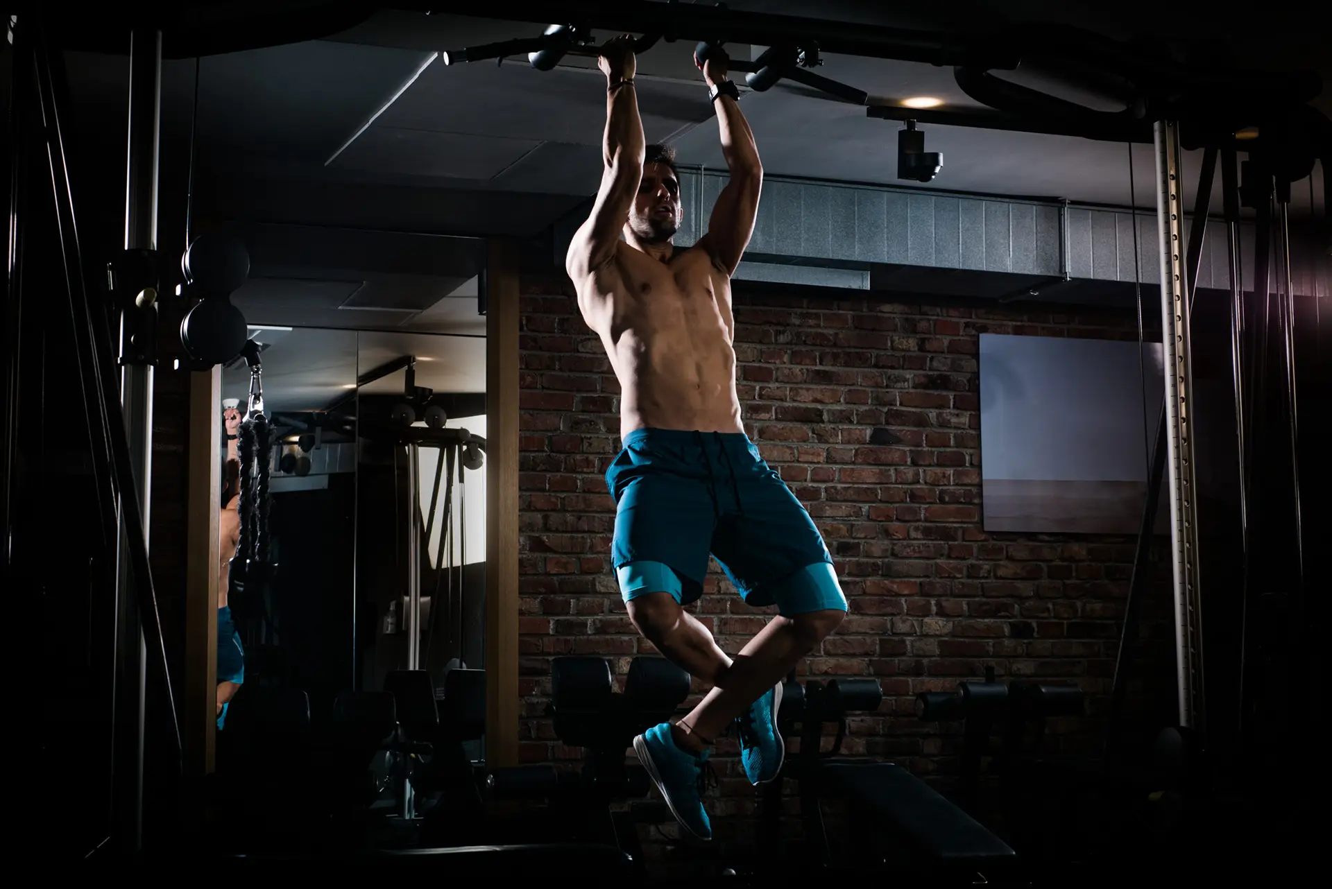 Sportlicher junger Mann macht Klimmzüge im dunklen Fitnessstudio – 24/7 Training mit flexiblem Zugang.