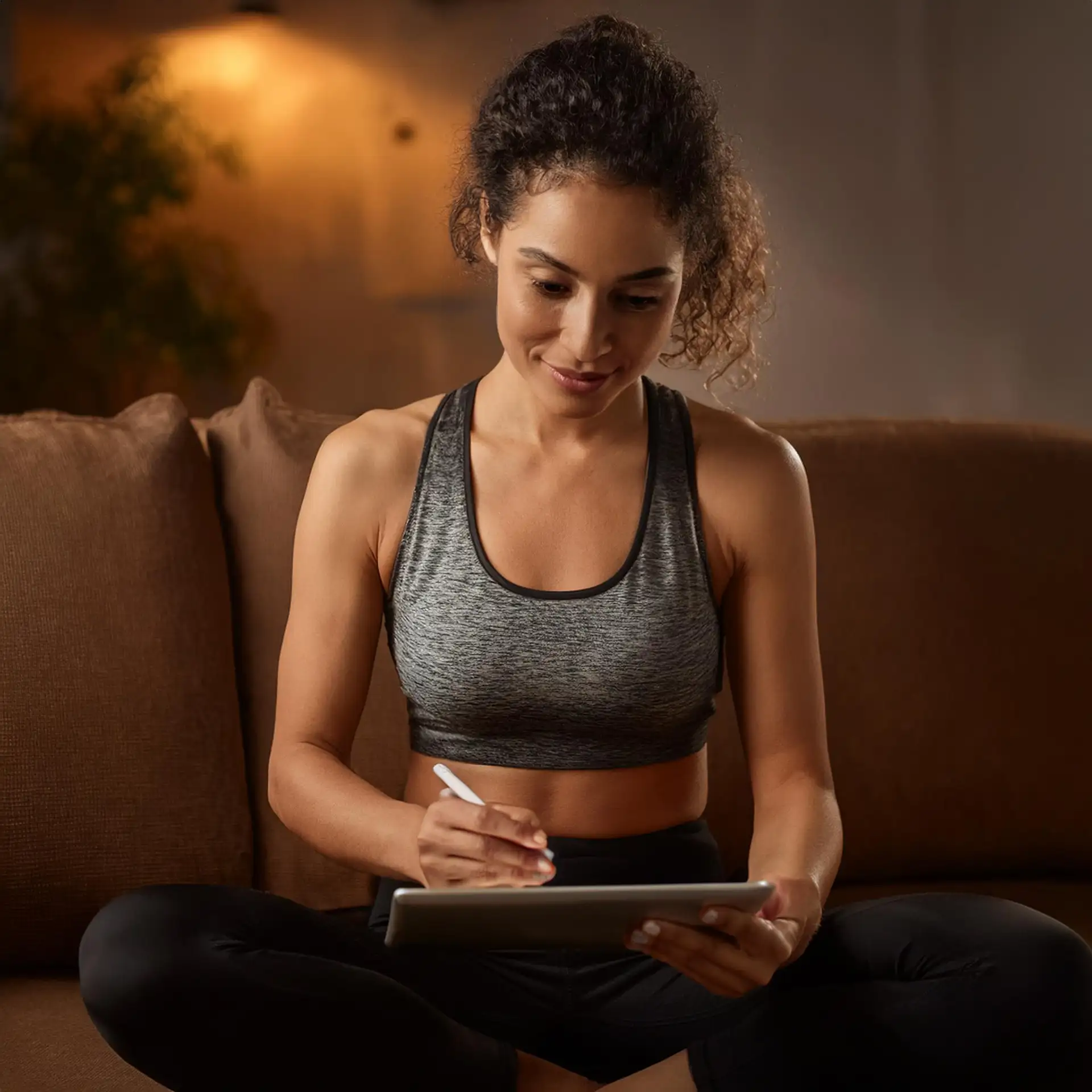 Eine junge Frau in Sportkleidung unterschreibt einen digitalen Fitnessstudio-Vertrag auf einem Tablet – einfacher Online-Vertragsabschluss von zu Hause.